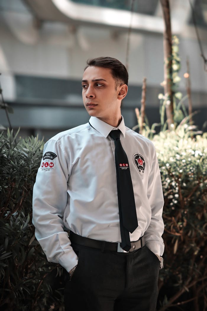 A security guard in uniform stands confidently outdoors, looking to the side.