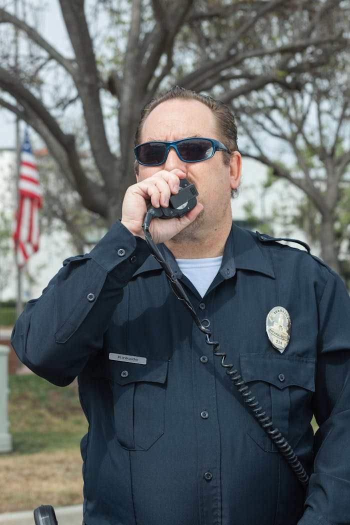 Portrait of a police officer using a walkie-talkie outdoors, wearing sunglasses and uniform.